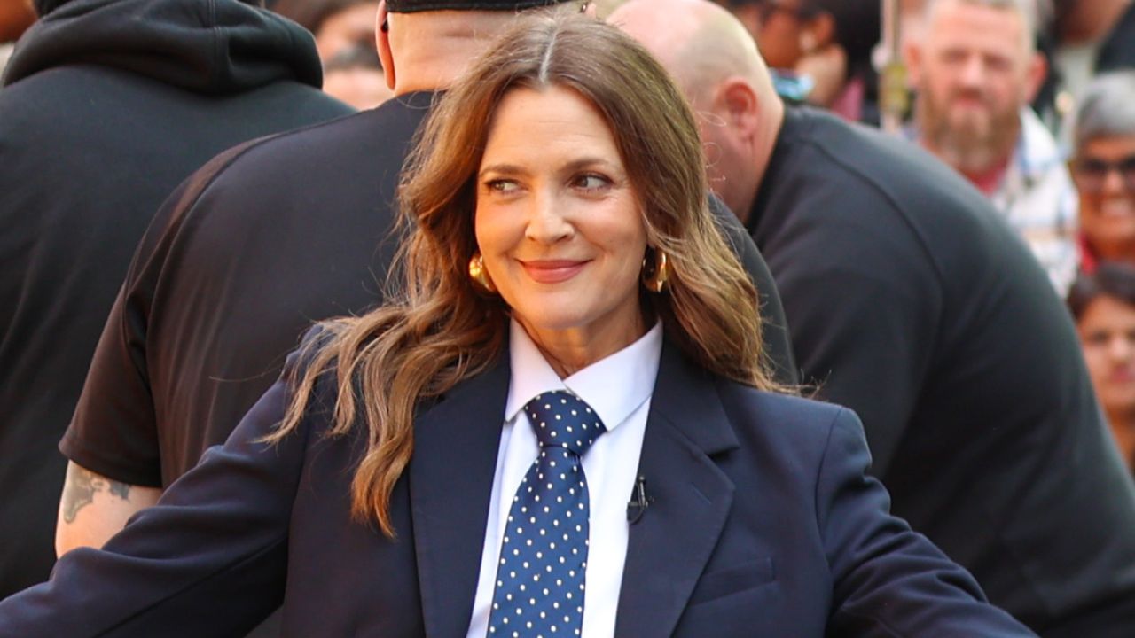 Drew Barrymore poses outside while wearing a dark blue suit with a white shirt and a blue and white polka dot tie