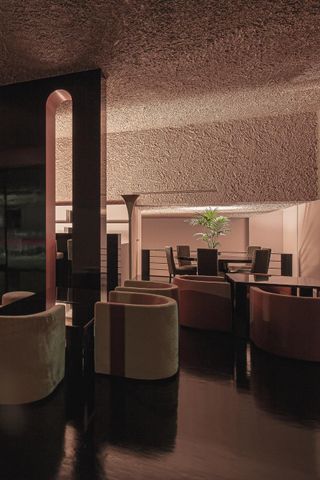 The dining room at Off Club restaurant, with tub chairs and elongated copper arches, glossy black floor