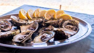 Oysters open on a plate on the beach with slices of lemon