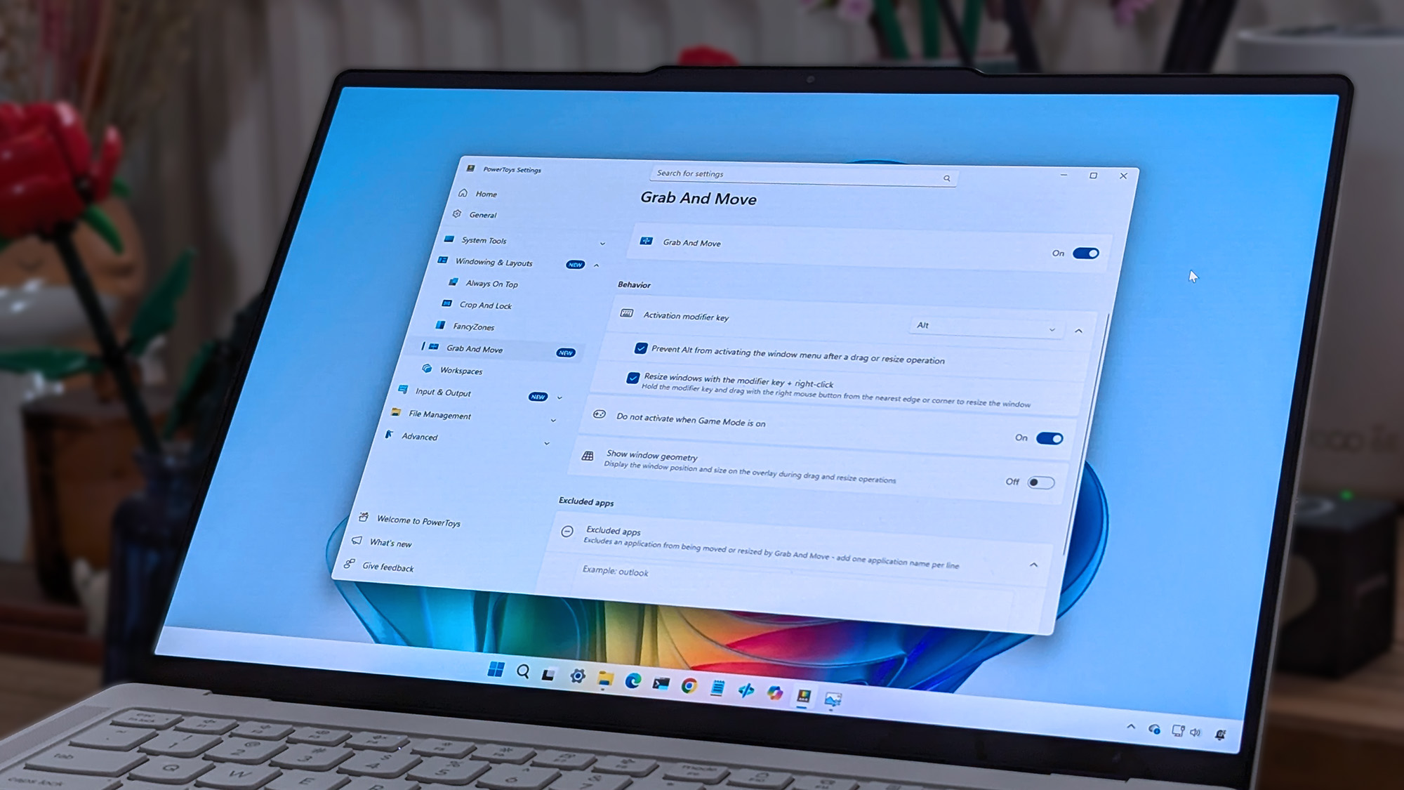 A laptop screen displaying Windows 11, featuring the "Grab And Move" settings window of PowerToys. The desktop background is colorful and vibrant.