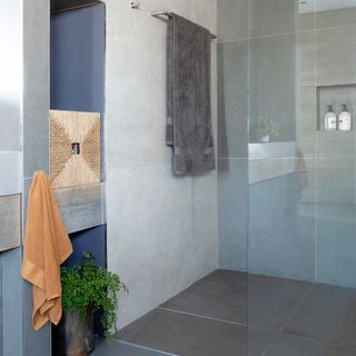 A modern bathroom with extralarge grey wall tiles and shower enclosure with glass door and recess shelf area