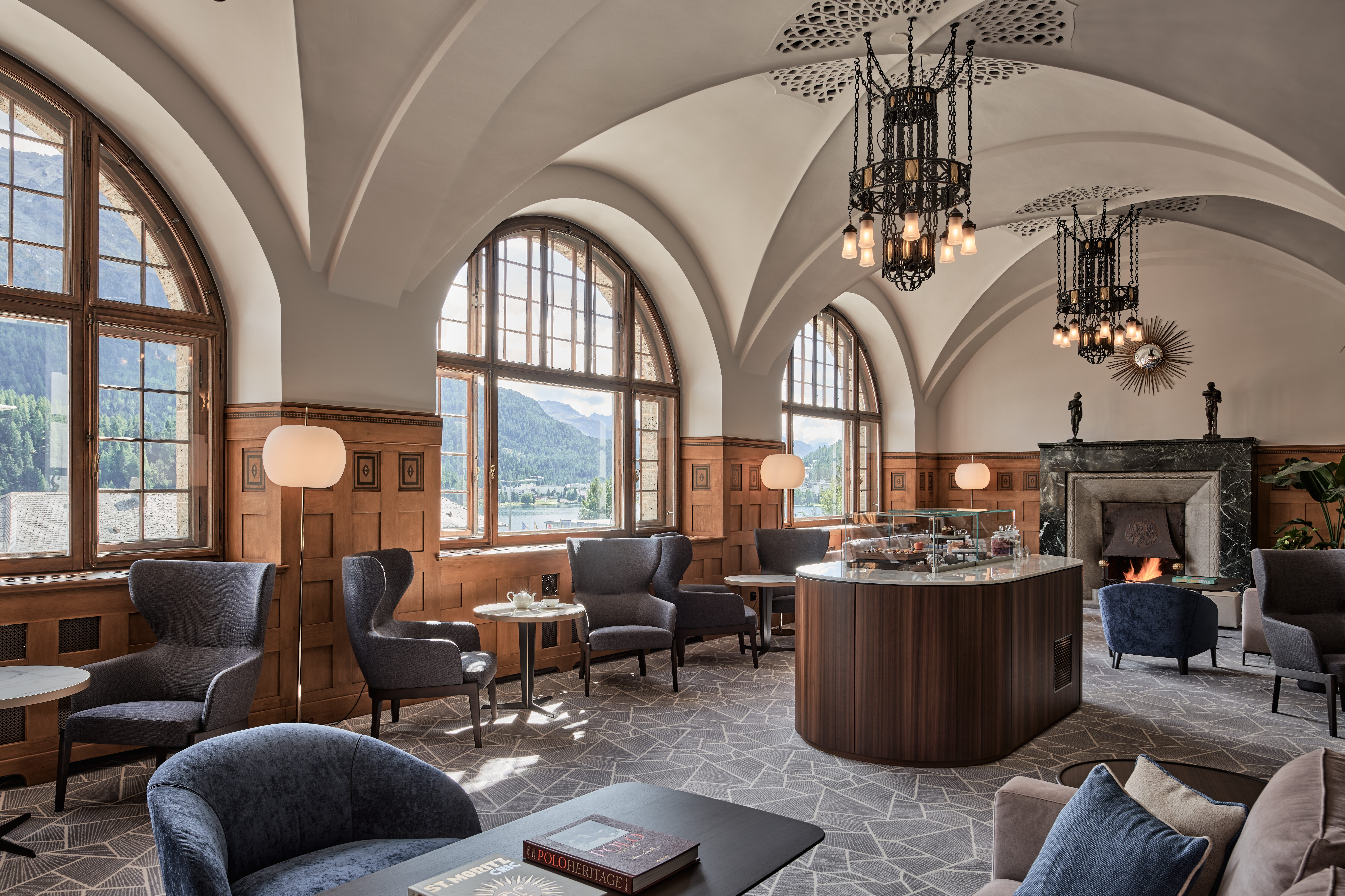 A mountain chalet's bar features terrazzo flooring, wooden finishings, and a number of Art Nouveau touches, including wrought iron chandeliers, all encircled by arched, wide windows.