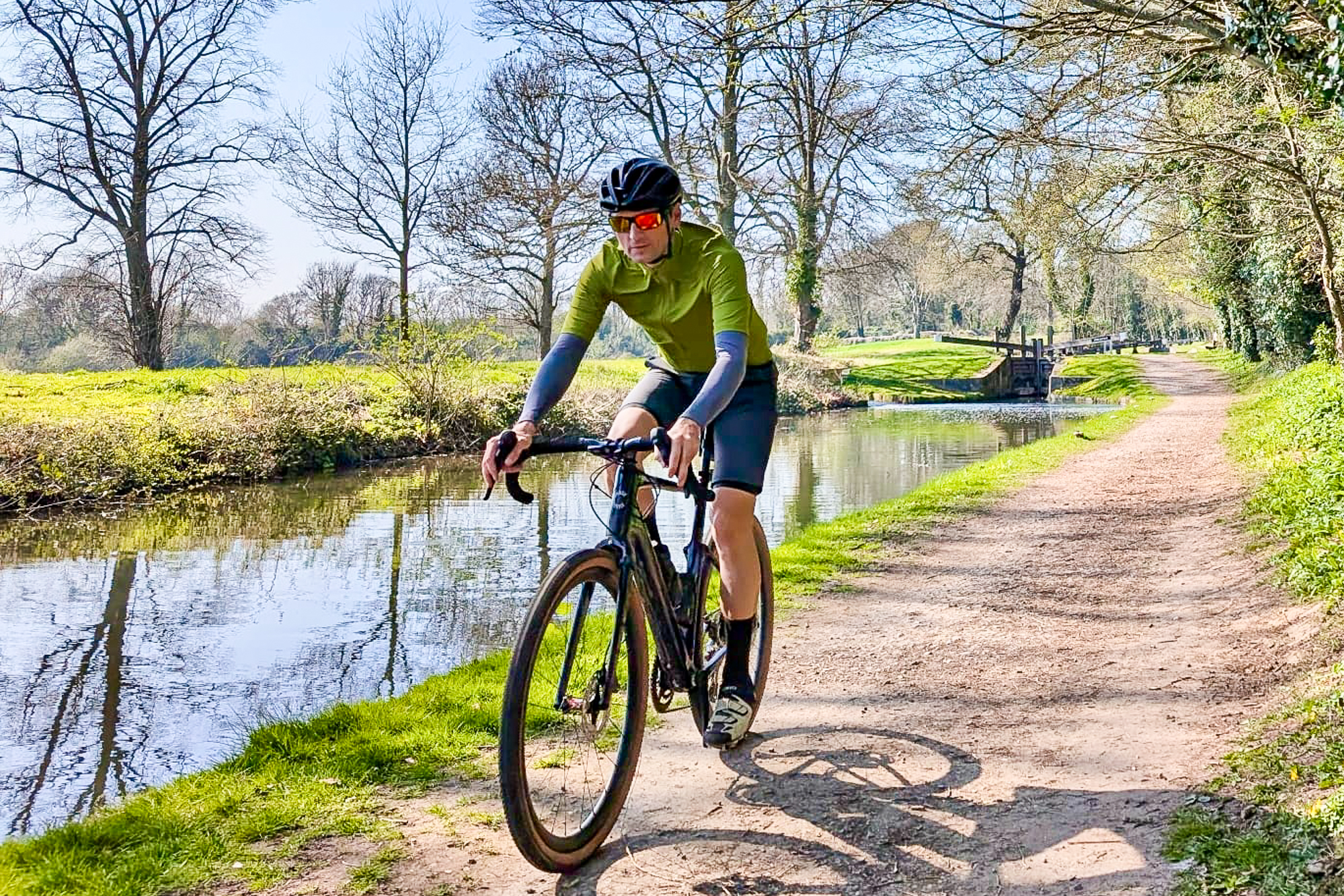 Man riding along a canal towpath wearing a green jersey and black helmet