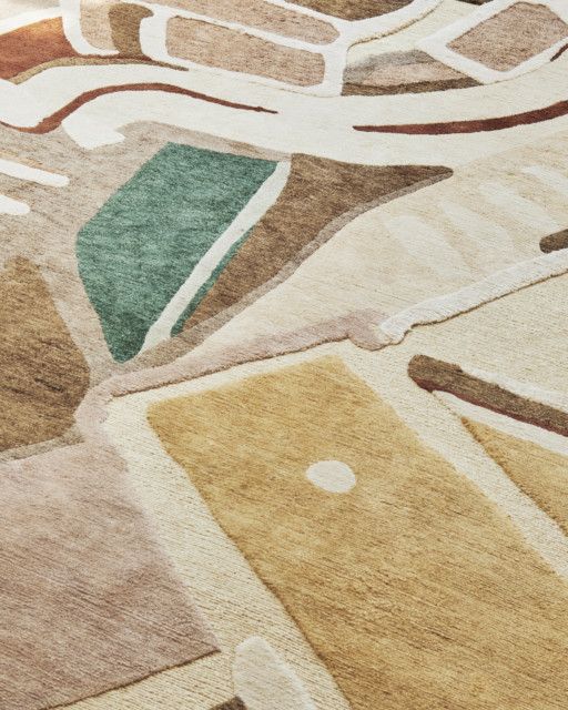 A detail of a pastel-shaded rug features abstract shapes in the tones of sand, pale pink, green, brown, orange, and white.