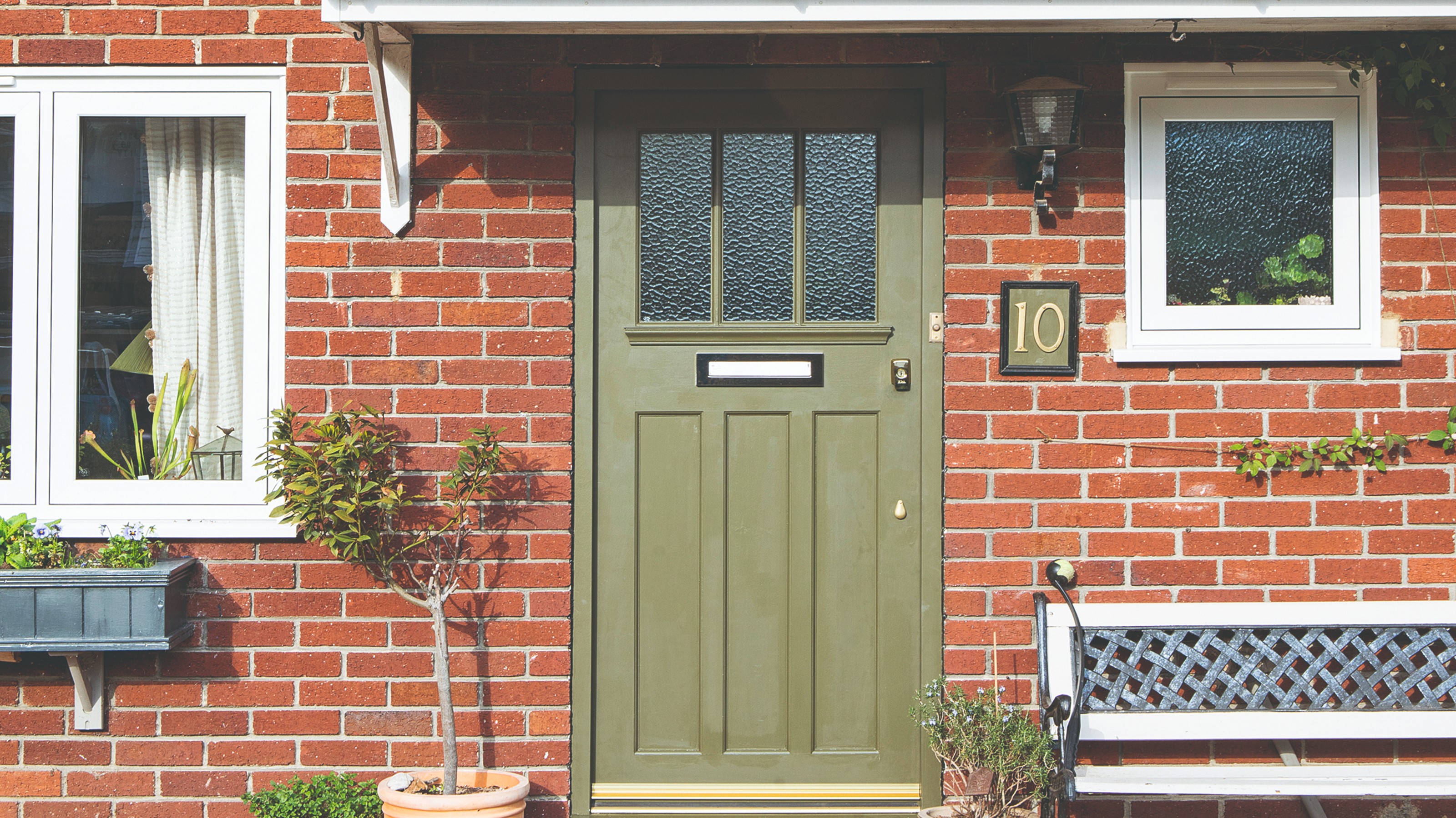 A front porch with an olive green front door and a garden bench for seating