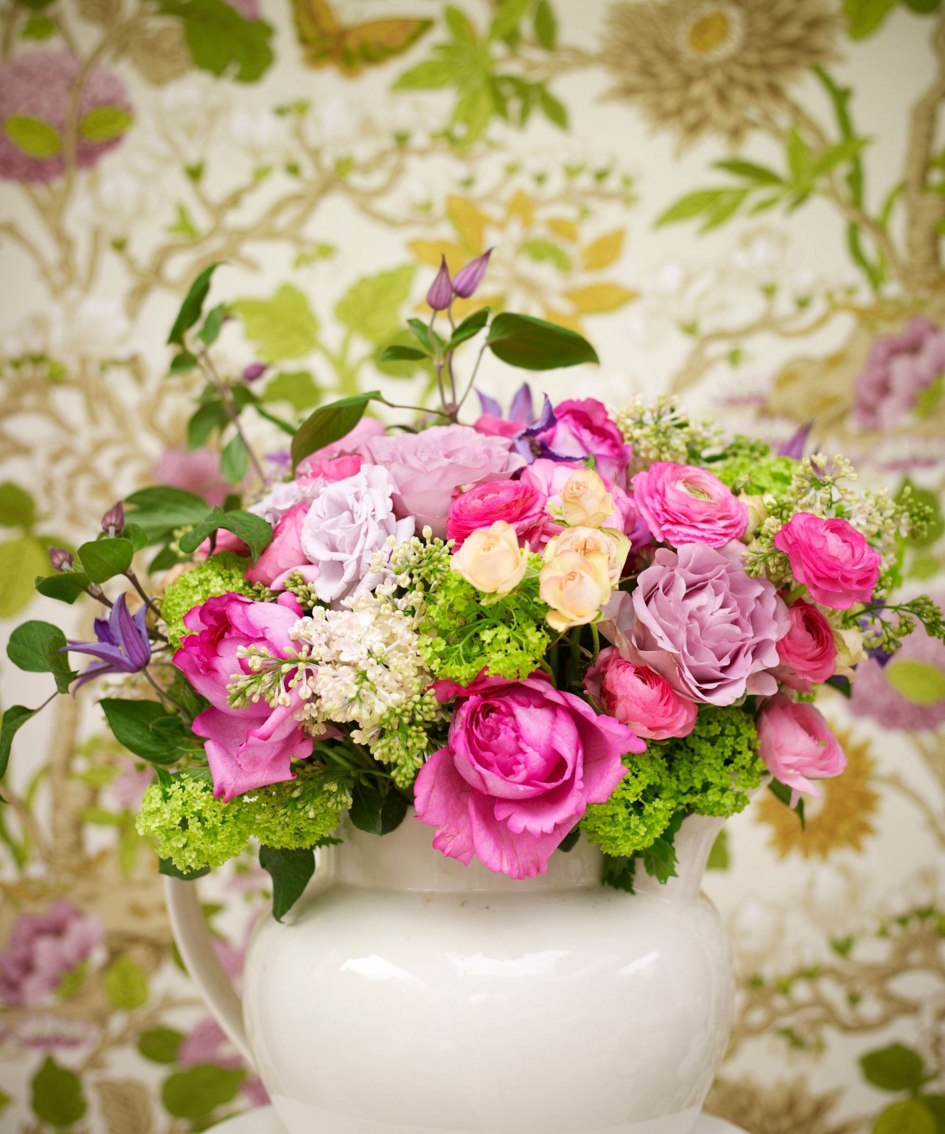 Bright pink and green flower arrangement in a white jug with botanical wallpaper in the background