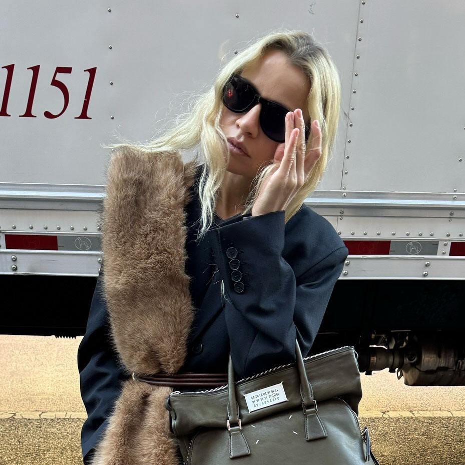 a woman wearing a fur scarf, black coat, and green bag