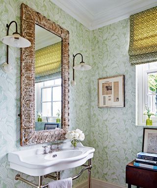 A bathroom with green and white wallpaper and a grand mirror above a traditional sink