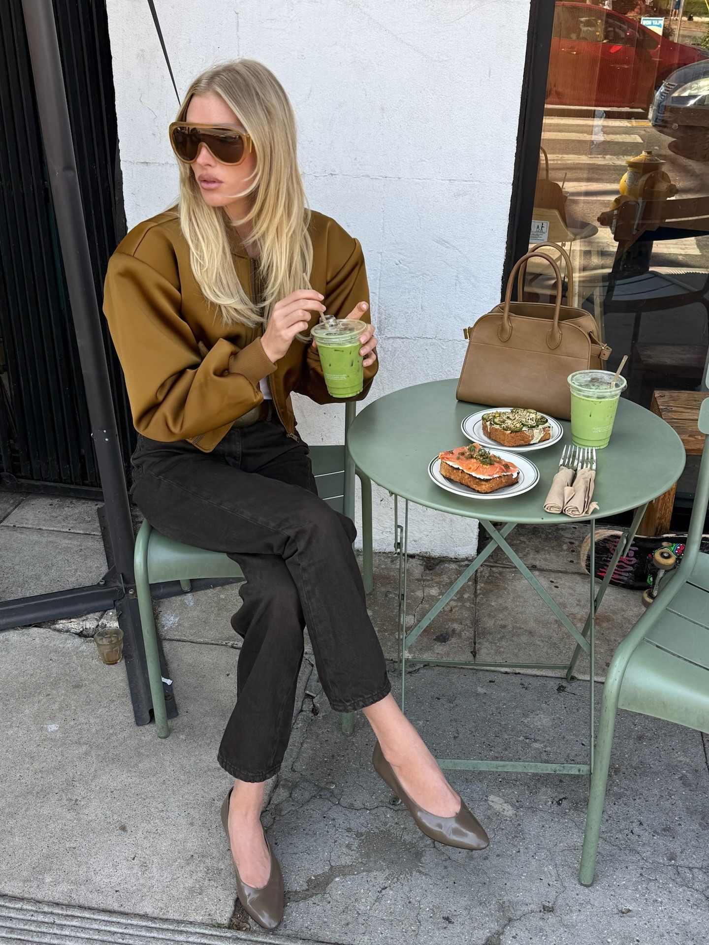 Elsa Hosk wearing a tan bomber jacket, brown jeans, and olive green shoes