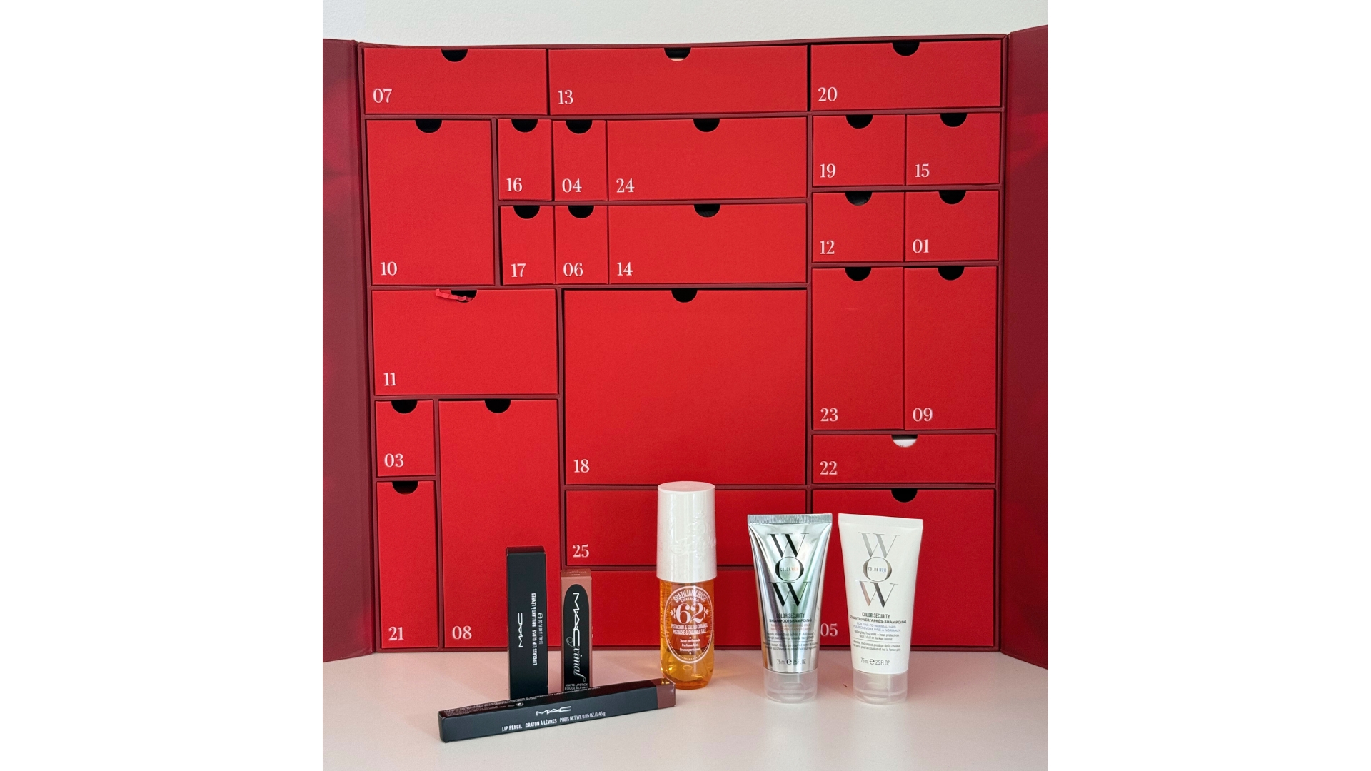 The red LookFantastic Beauty Advent Calendar 2025 with some of its contents stood in front of it (L-R) MAC trio of lip products, Sol de Janeiro&#039;s Cheirosa 62 and Color Wow&#039;s Color Security Shampoo and Conditioner