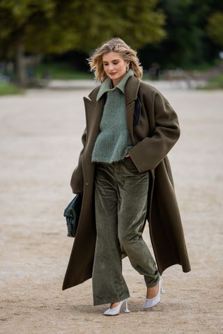 Woman in green corduroy pants, sweater, and coat.