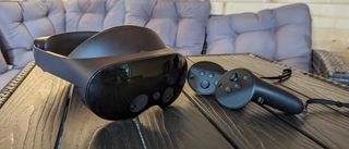 Ett Meta Quest Pro-headset ligger bredvid sina tillhörande kontroller på ett mörkt träbord, med en grå soffa i bakgrunden.