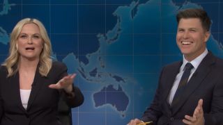 Colin Jost laughs while Amy Poehler makes a joke on Weekend Update.