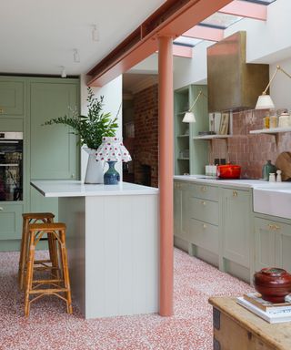 Mint green kitchen with pale orange painted metal beam, terrazo floor, island, bar stool