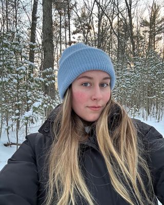 Beauty editor Kaitlyn McLintock outside in the snow wearing a blue beanie and a black coat.