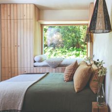 A bedroom with panelled storage surrounding the window with a built-in window seat and the bed dressed in linen bedding
