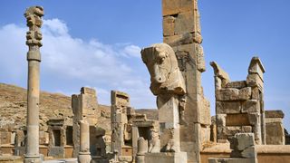 Iran, Fars Province, Persepolis, World Heritage of the UNESCO, pillars of the Apadane palace. tall stone pillars rise high against the blue sky. There appears to be a horse head carving on the nearest one.