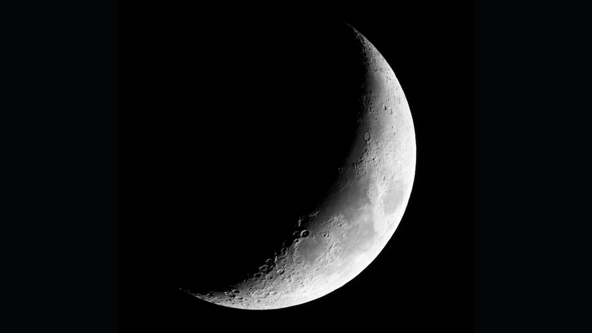 A waxing crescent moon is pictured with its right side lit by sunlight and its left hidden in shadow against a black sky.