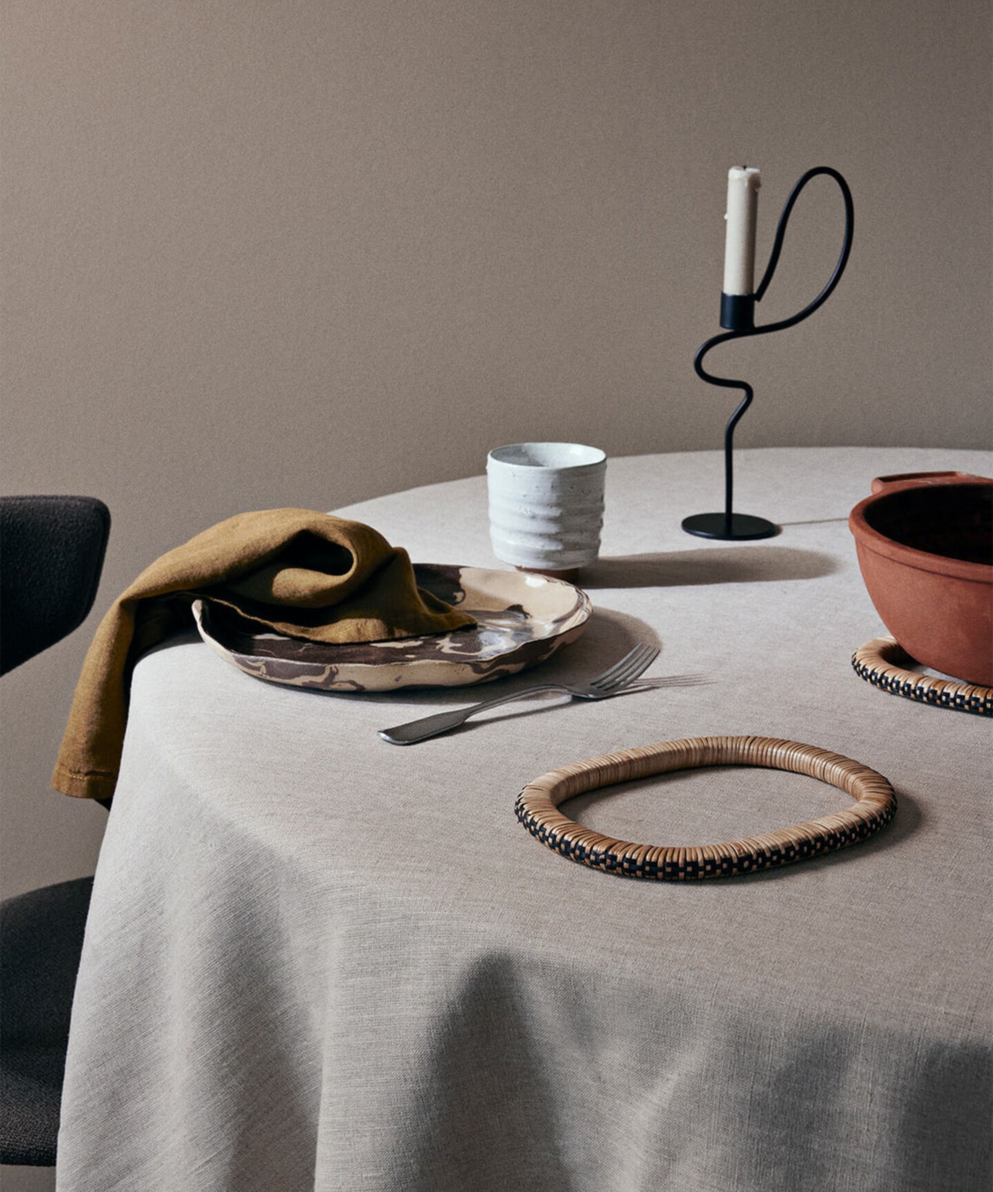 round table with linen tablecloth with ceramic dinner plate with linen napkin, silver folk, candlestick and ceramic mug, and trivet