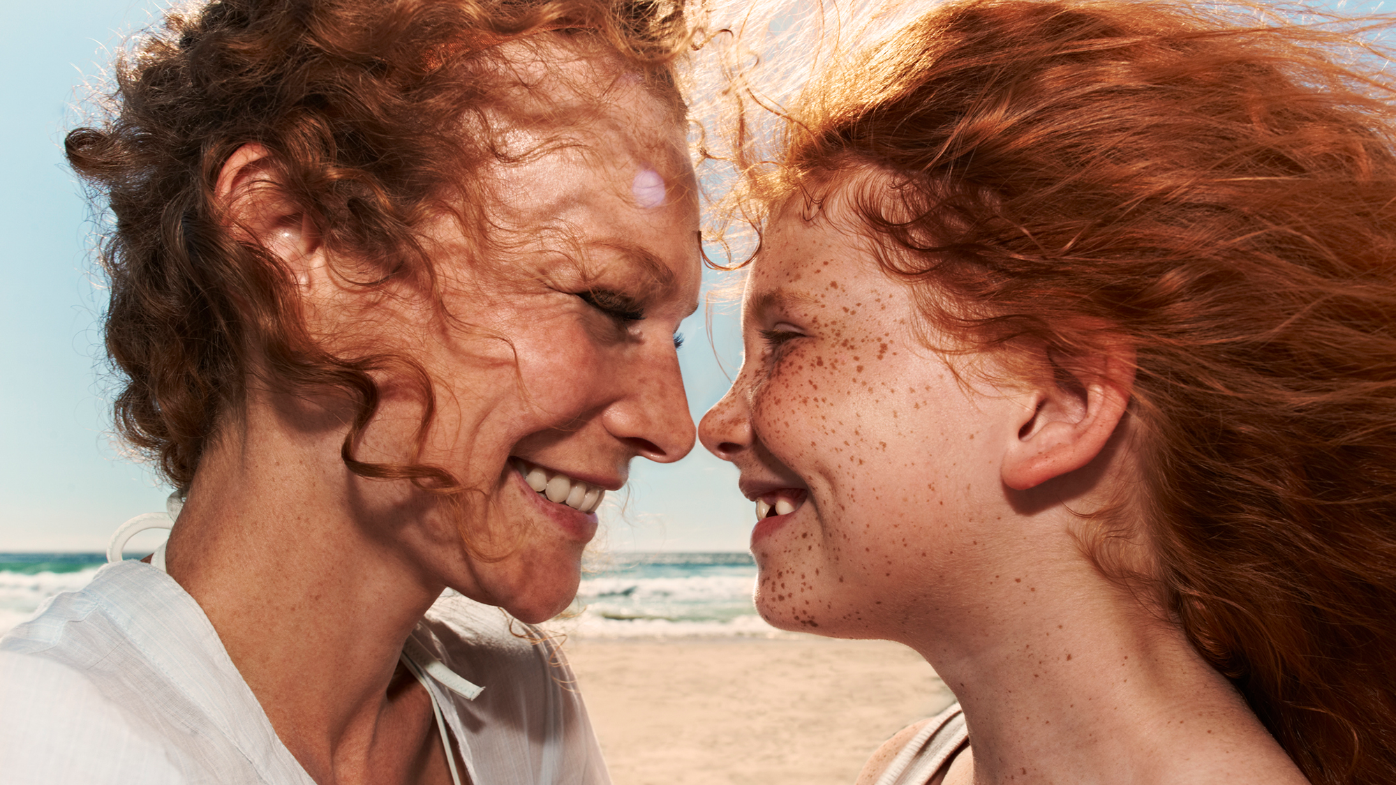 A mother with curly red hair smiles at her daughter, also with curly red hair