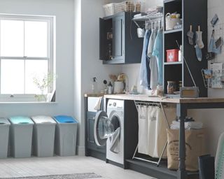 a grey and white utility laundry room with storage everywhere, including multiple floor bins, laundry baskets, and hanging pegs for clothes