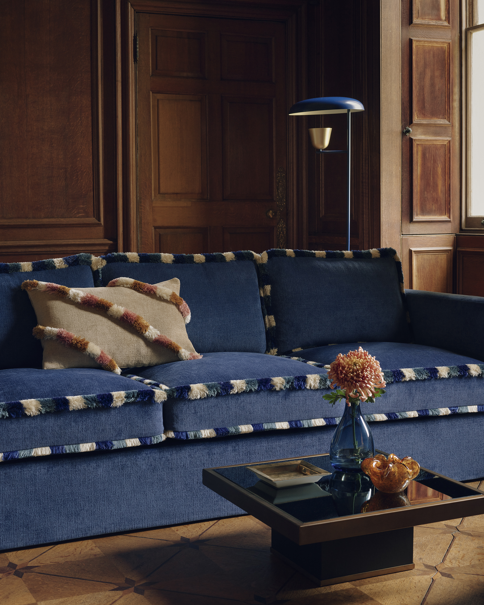 Image of a living room with wooden walls and a large denim blue sofa with white and blue tufted trim.