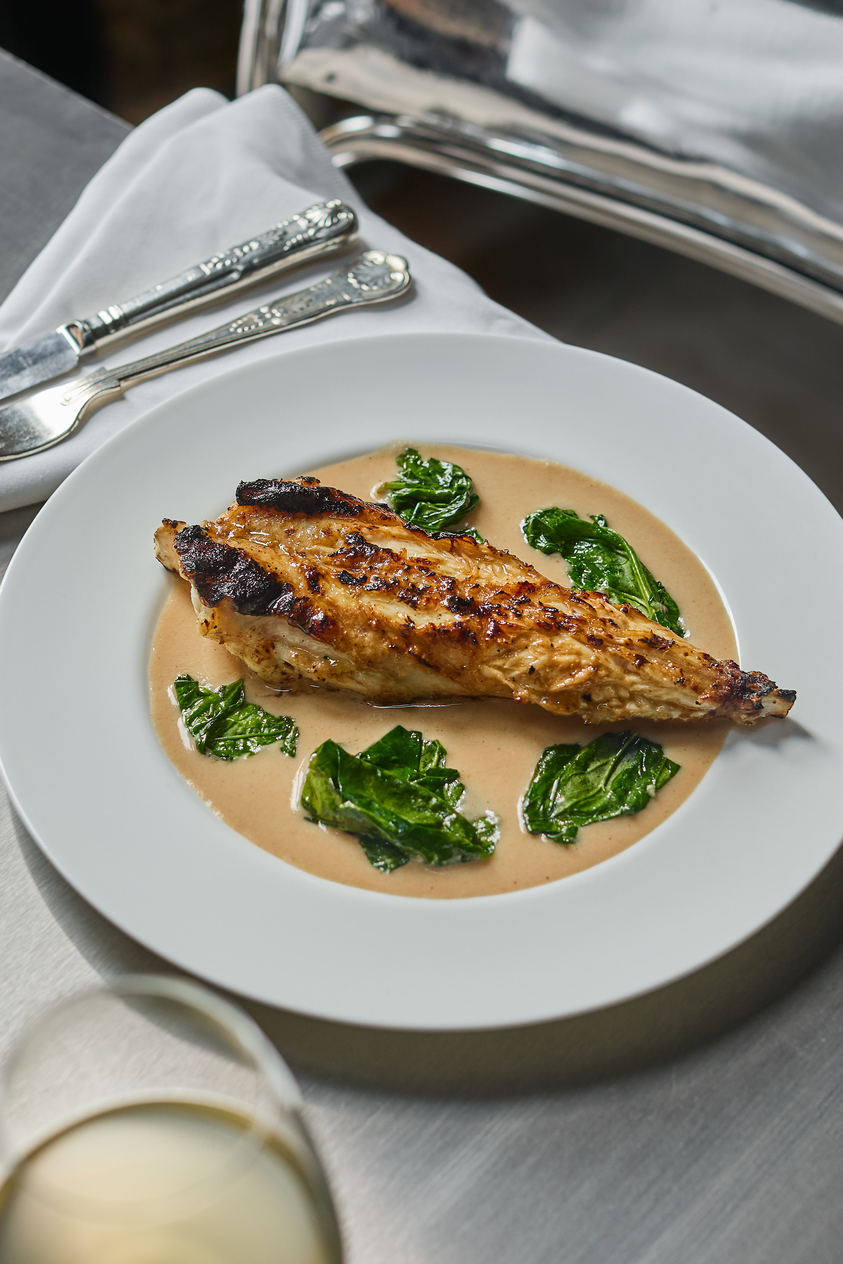 A series of beautifully presented, colorful restaurant plates and cocktails come served in white or chrome tableware and are placed atop silver tables.