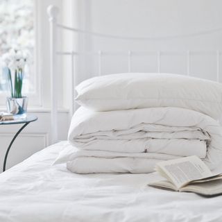 A white-painted bedroom with a white metal bed and a bedding set folded on top of it