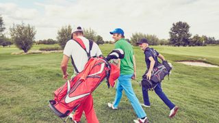 Three men on a golf course laughing carrying the best golf bags across the course