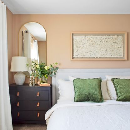 A bedrom with peach walls and a mirror beside the bed