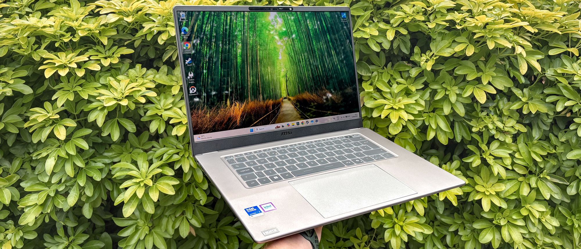 MSI Prestige 16 AI+ being held in hand with green bush in background
