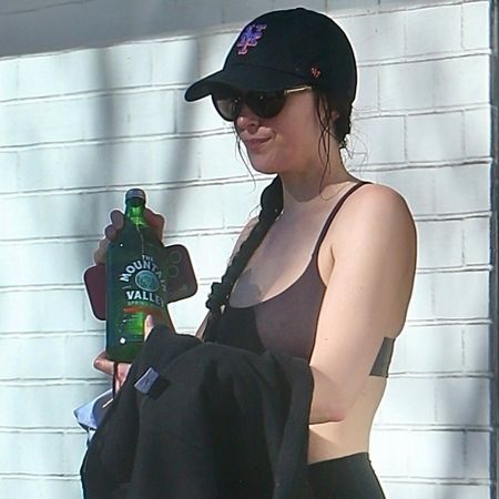 Dakota johnson wears a mets hat, burgundy sports bra, black leggings, and black nike sneakers while carrying a moutain valley water bottle.