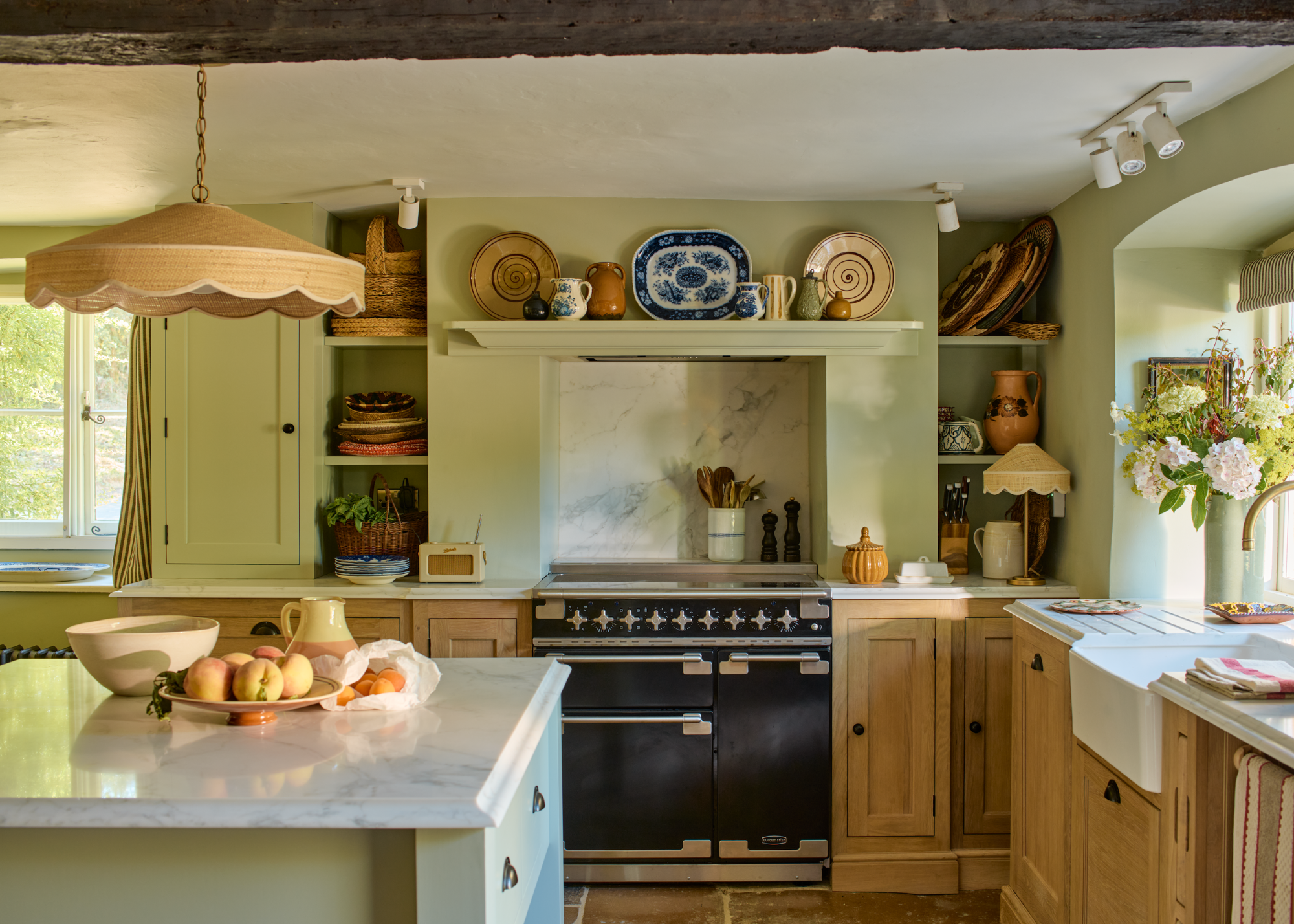 A traditional period kitchen in a light green and light yellow with a cooker and open shelving above and to the side featuring decorative plates