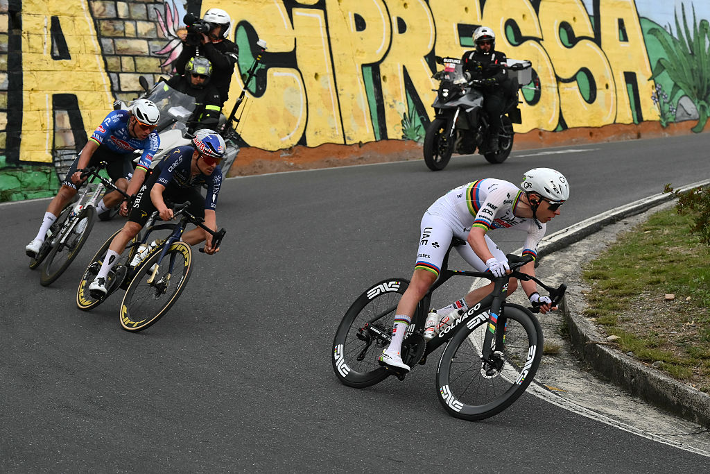 Tadej Pogacar leads Tom Pidcock and Mathieu van der Poel down the Cipressa in front of the spray painted mural that says Cipressa
