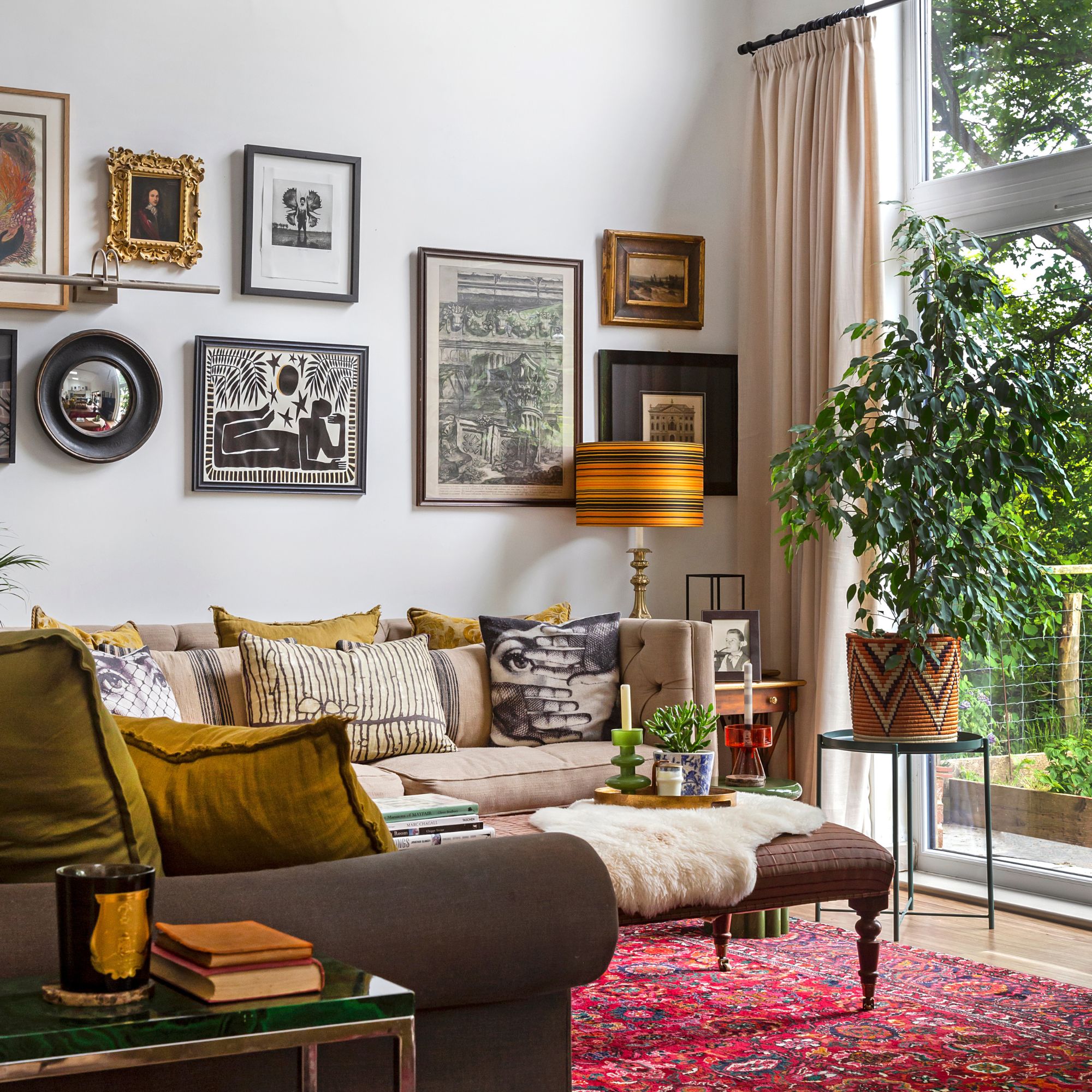 Gallery Wall Living Room With Red Patterned Rug, Gray Sofa With Green Cushions And Greenery