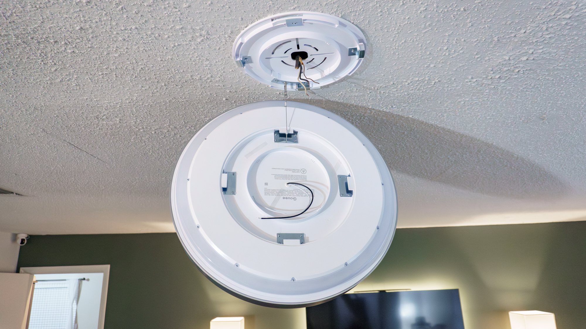 The Govee Ceiling Light Ultra connected to its mounting plate via a wire and hanging in the air before the final installation