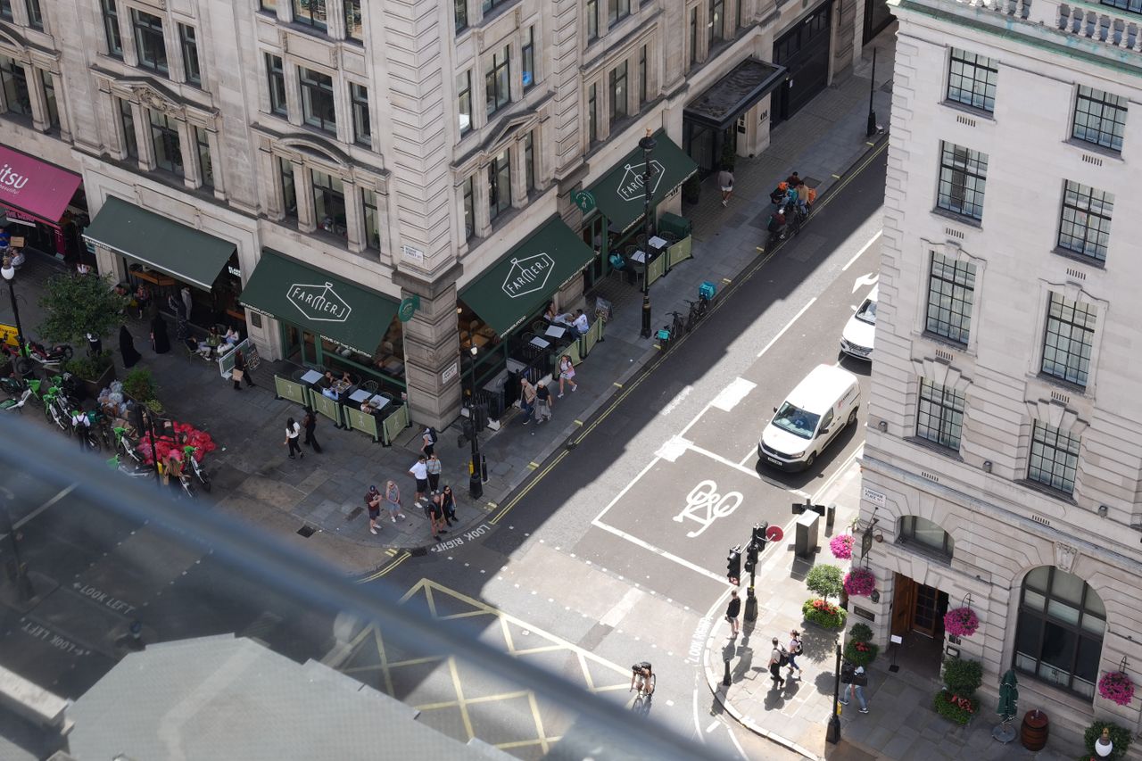 Elevated view of a London street corner with restaurants, pedestrians, cyclists, and traffic.