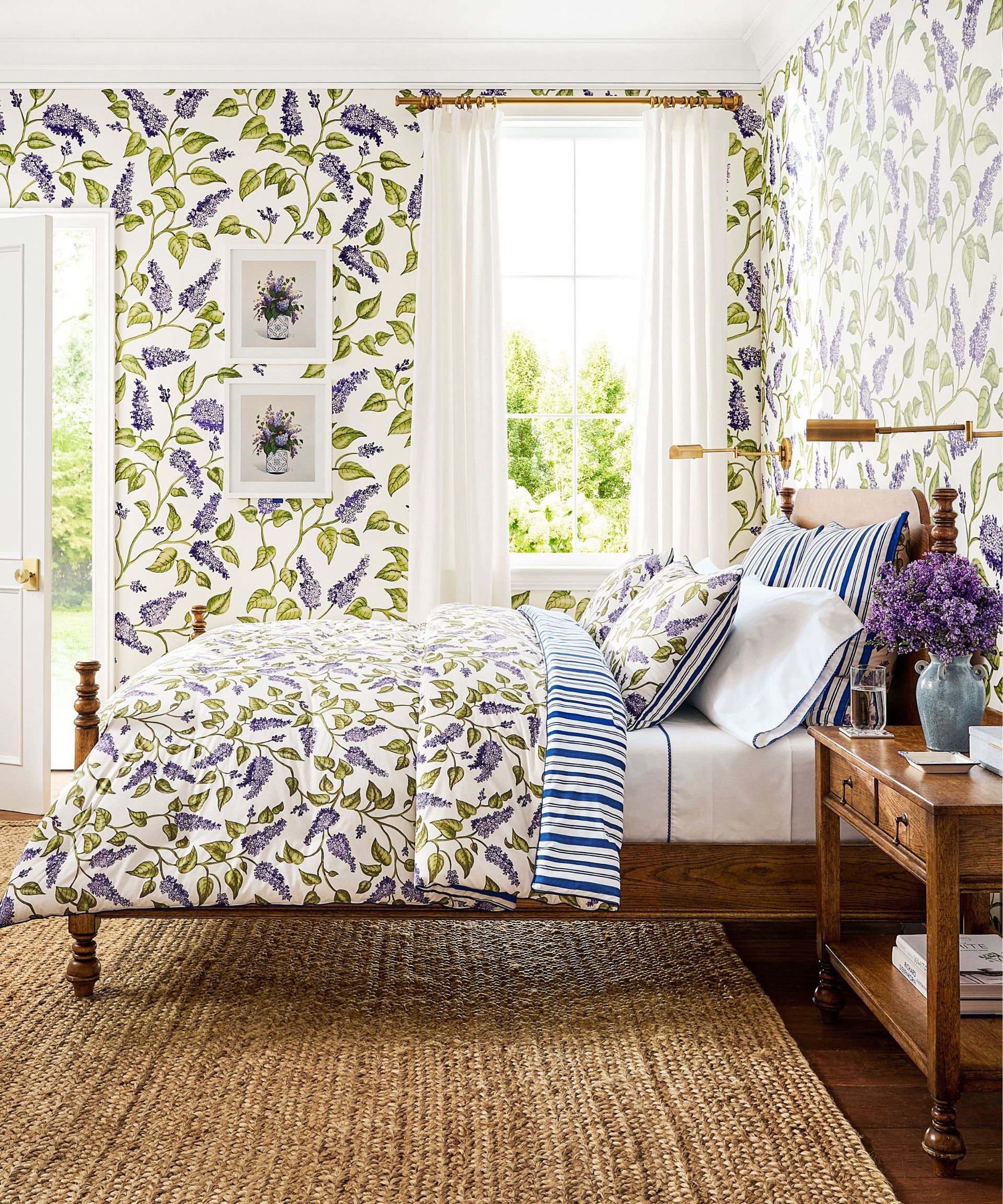 bedroom styled for the Mark D. Sikes x Pottery Barn collaboration with lilac print wallpaper and bedding with a rattan rug and dark wooden furniture