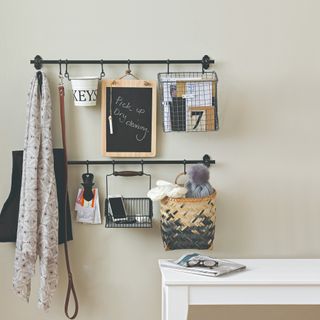 A hallway with an off-white wall, a white bench and two hanging rails attached to the wall