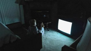 A still from the movie Skinamarink, showing two children sat on the carpet in front of a TV