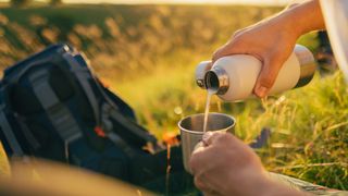 a person pouring tea from a insulated bottle into a cup