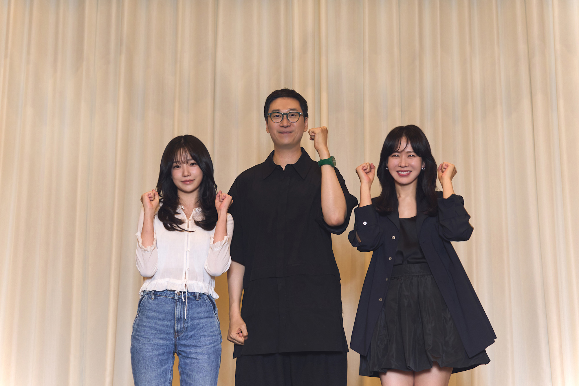 Actress Jo Yu-ri, director Kim Yong-hoon, and actress Son Ye-jin pose in front of a ivory curtain. The trio raise their fisted hands over their shoulders in the Korean gesture of encouragement (a.k.a. "Hwaiting!")