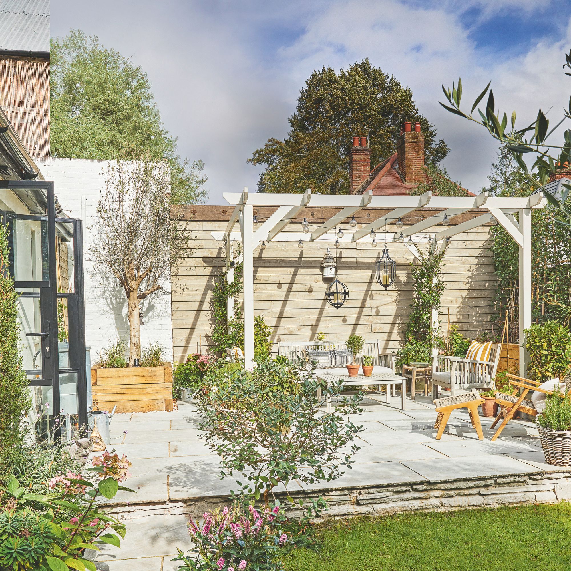 Outdoor seating area with cushions beneath wooden pergola with festoon lights and hanging lanterns