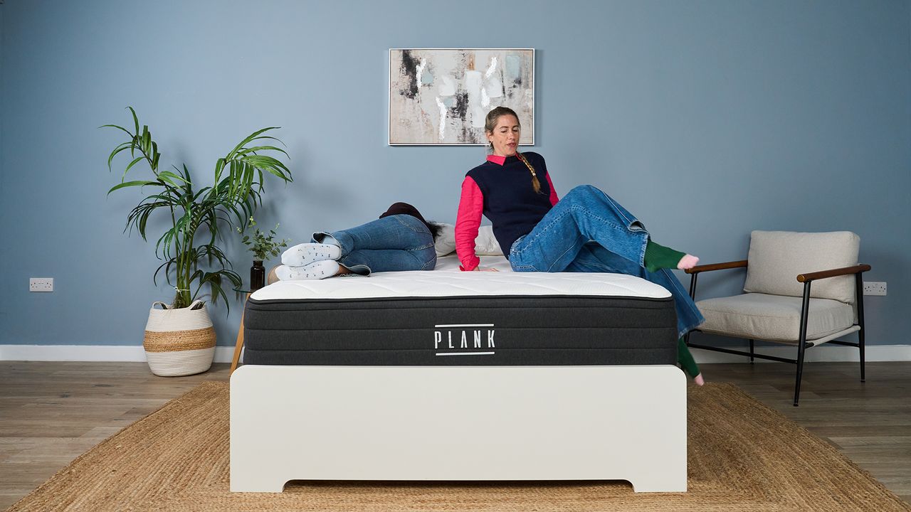 Mattress tester Becky George lies on the left side of the Plank Firm Luxe mattress as tester Nicola Appleton climbs onto the right side, testing motion isolation and comfort