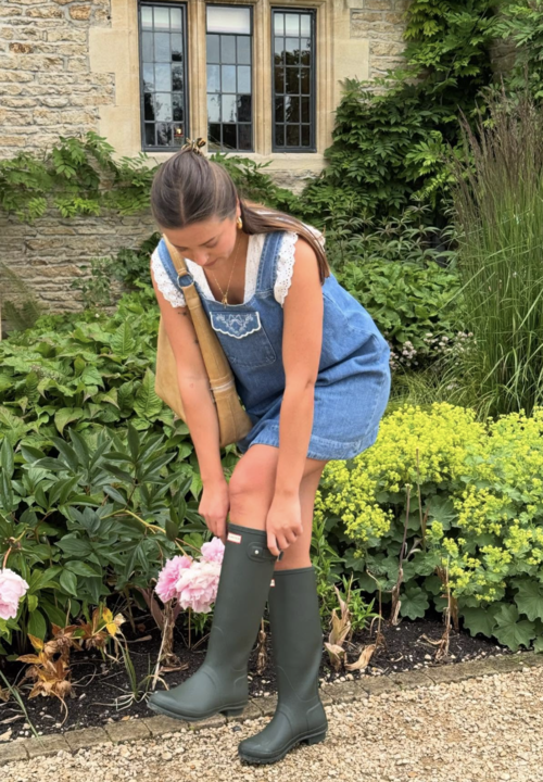 Fashion person Olivia Heering wears a denim blue mini dress and ruffled v-neck top and green hunter wellies, she is carrying a beige suede hobo bag in a image taken from her Instagram recently.
