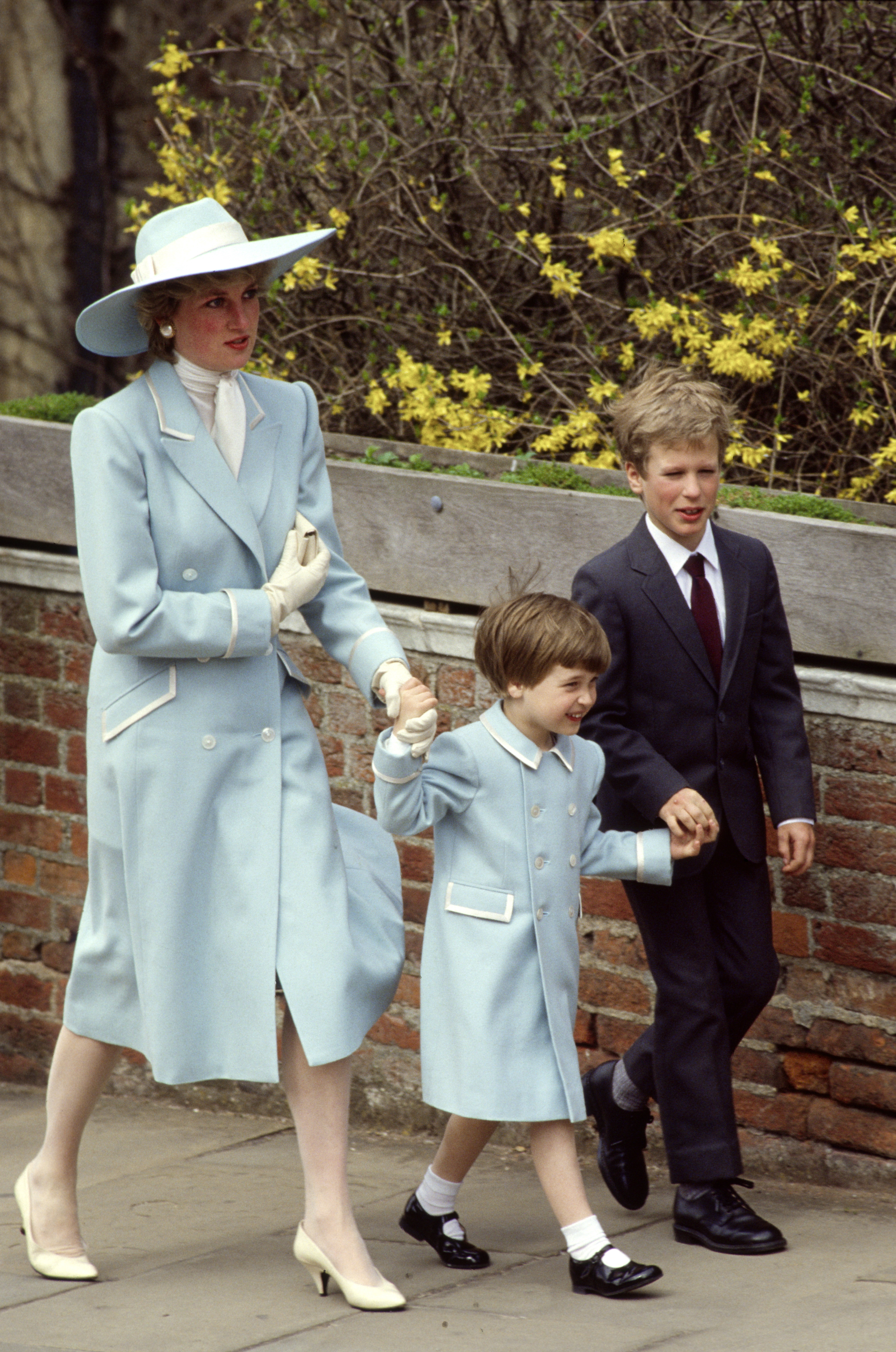 Princess Diana holding hands with Prince William in a blue coat