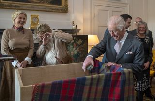 King Charles putting things into a box while Penny and Rod Stewart stand behind him and Rod covers his face