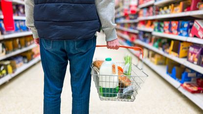 A man faces a grocery aisle with a shopping basket in hand.