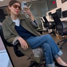 Woman in trench coat, navy sweater and jeans