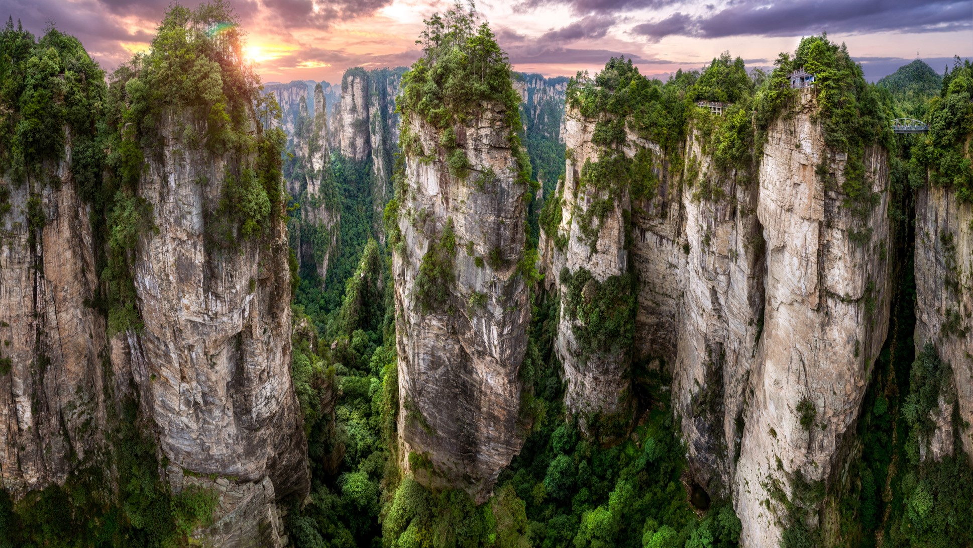 huge towering rock formations rise from the forests below, the formations are also covered in trees and vegetation.